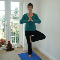 Cathie in tree posture and hands in prayer position infront of the heart space. In Tree we are deeply rooted, balanced, connected to the heart and opening to the sky.